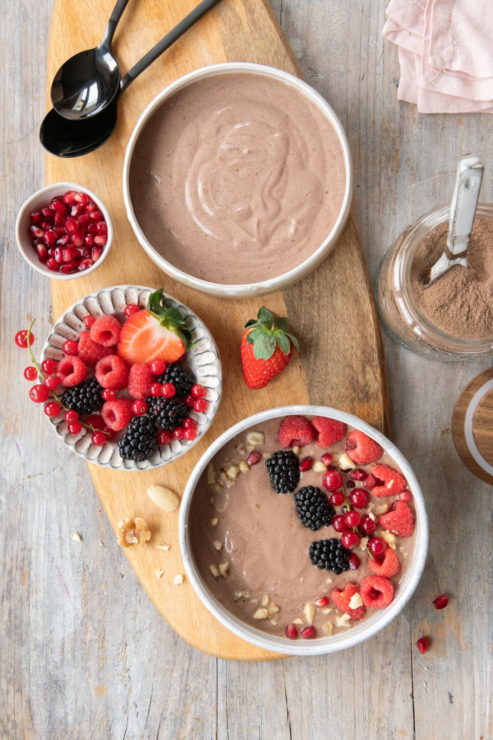 UNE Foods Premium Kollagen Hydrolysat mit Ballaststoffen und Mikronährstoffen untergerührt in Joghurt-Bowls mit frischen Beeren, Erdbeeren und Granatapfel auf Holztisch