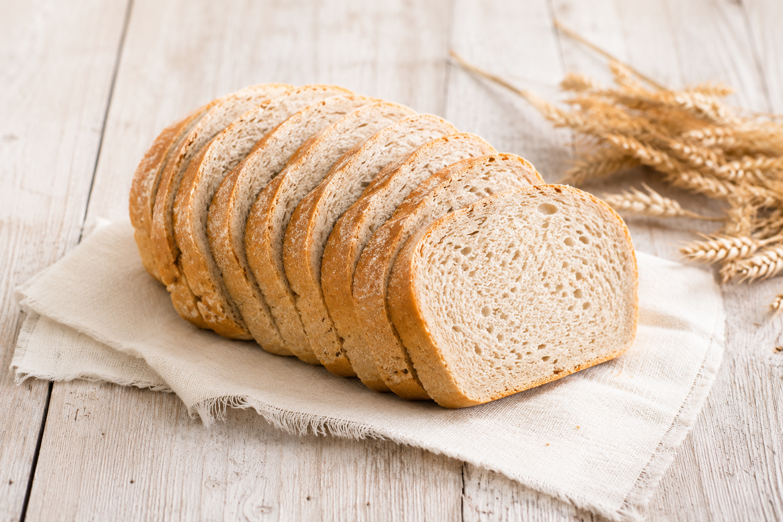 In Scheiben geschnittenes klassisches Weizenbrot auf hellem Leinentuch als Vergleichsbild für den Nährwertvergleich mit dem Low-Carb-Brot von UNE Foods.
