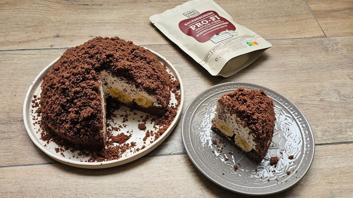 Maulwurfkuchen mit dunklen Schokokrümeln bedeckt, angeschnitten: Kuchenboden mit Sahne-Quark-Creme und Bananen gefüllt, auf weißem Teller